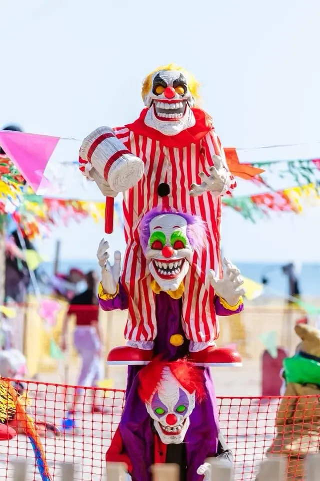 Three scary clowns are stacked vertically on a beach, each wearing a different clown costume with exaggerated makeup and…