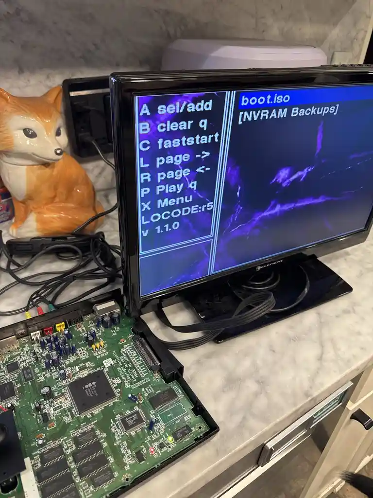 A computer monitor displays a retro-style boot menu with options like 'A sel/add', 'B clear q', and 'C faststart', while a…