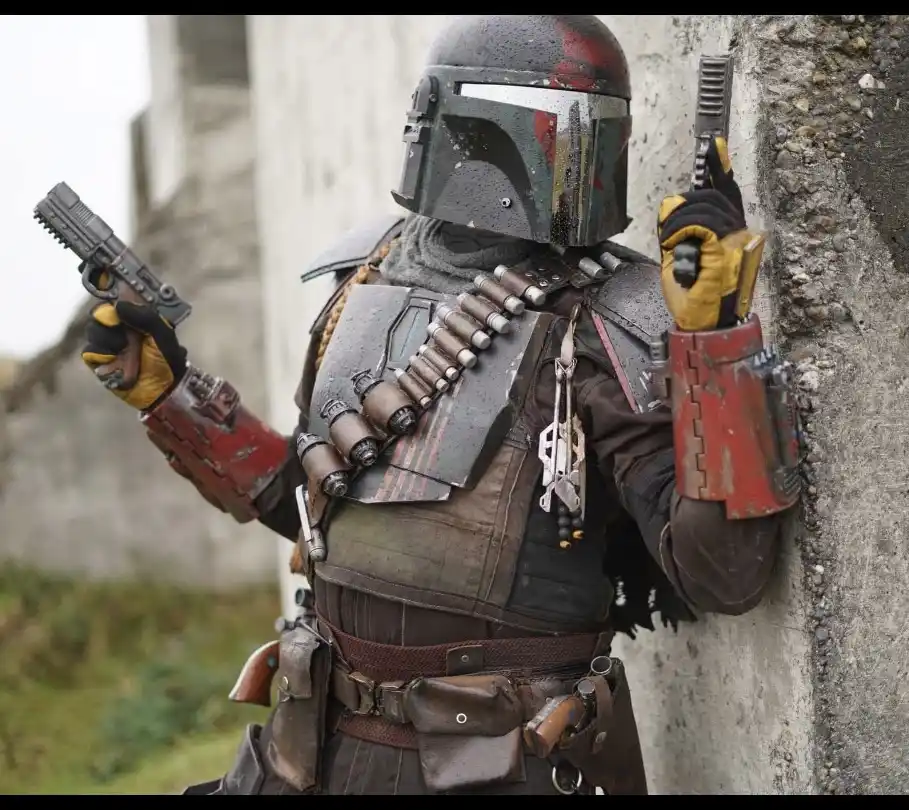 A character in Mandalorian armor, holding two blasters, leans against a concrete wall. The image has text overlaid that…