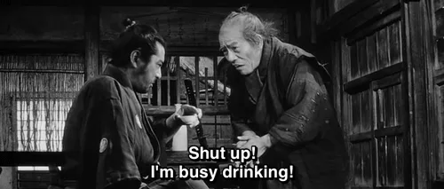 A black-and-white image from a Japanese film shows an older samurai repeatedly yelling at another man while holding a…