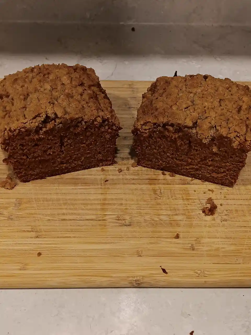 Two roughly square, dark brown baked goods, resembling dense coffee cake or quick bread, sit side by side on a well-used…