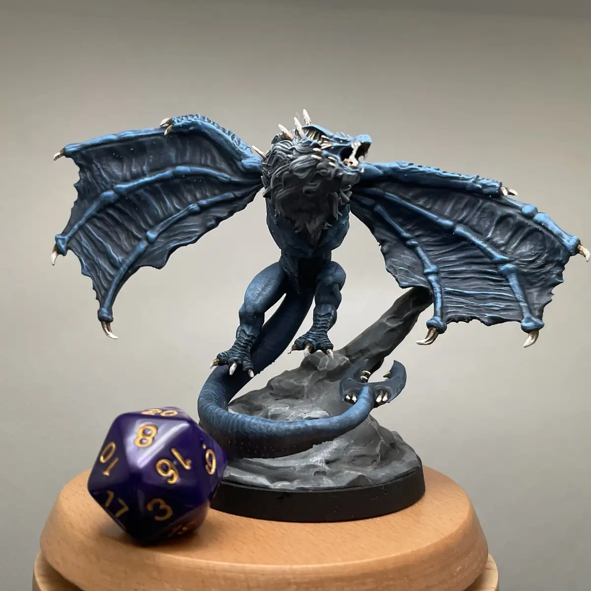 A dark blue, intricately detailed dragon figurine with spread wings and a coiled tail stands on a rocky base, positioned on…
