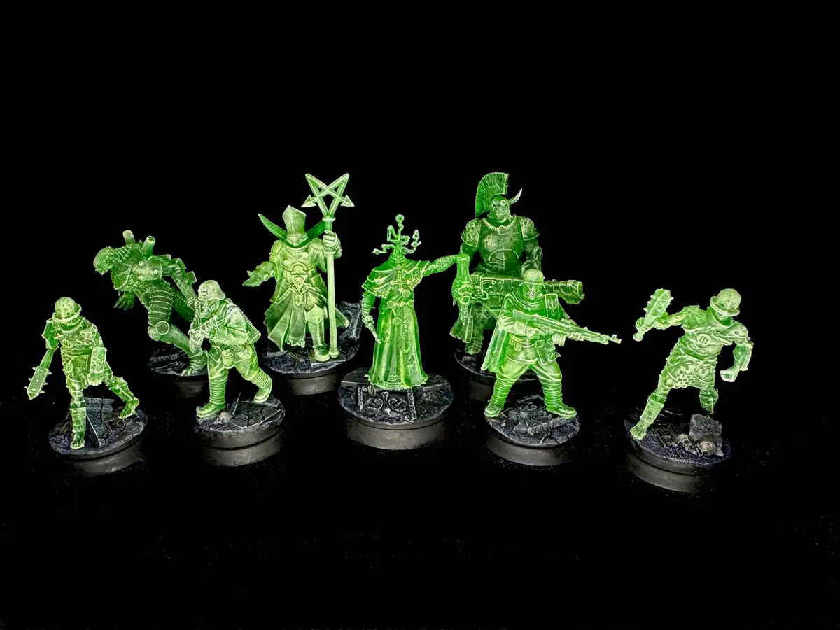 Seven translucent green miniature figurines of fantasy and sci-fi soldiers, warriors, and monsters stand on black circular…