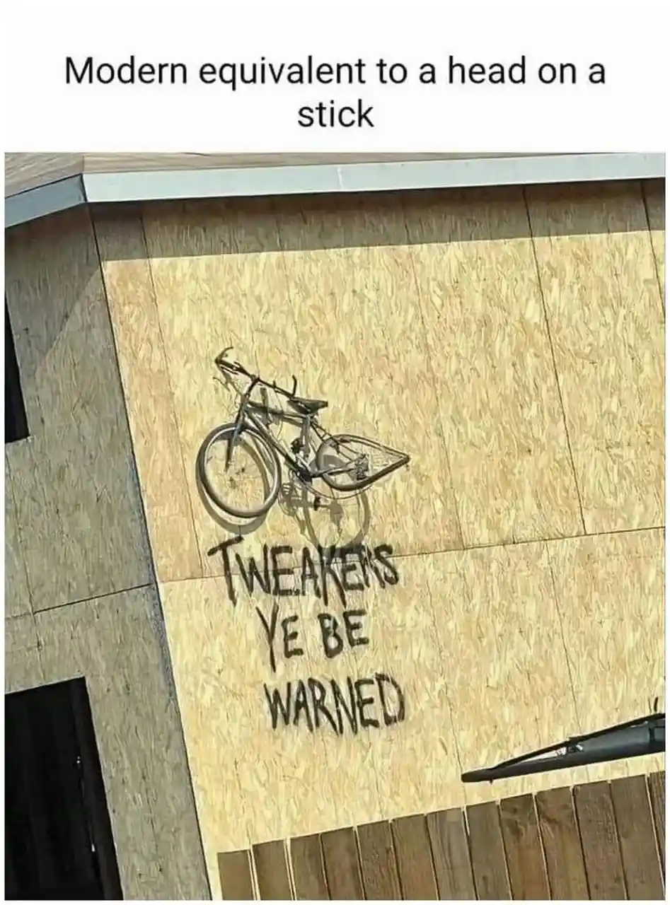 A photo shows a bicycle spray-painted on a plywood wall, with the words 'TWEAKERS YE BE WARNED' below it. The image is…