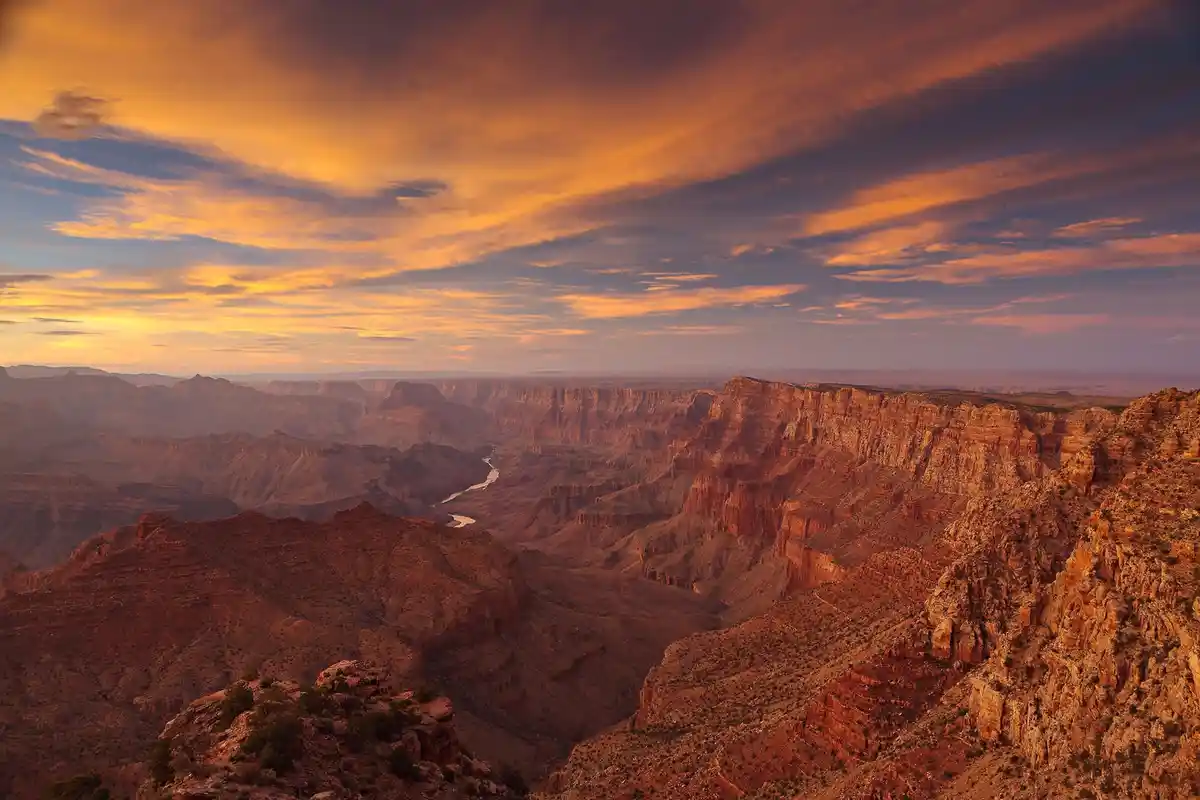 A breathtaking sunset photo of the Grand Canyon, showcasing vibrant orange and yellow clouds over layered red rock…