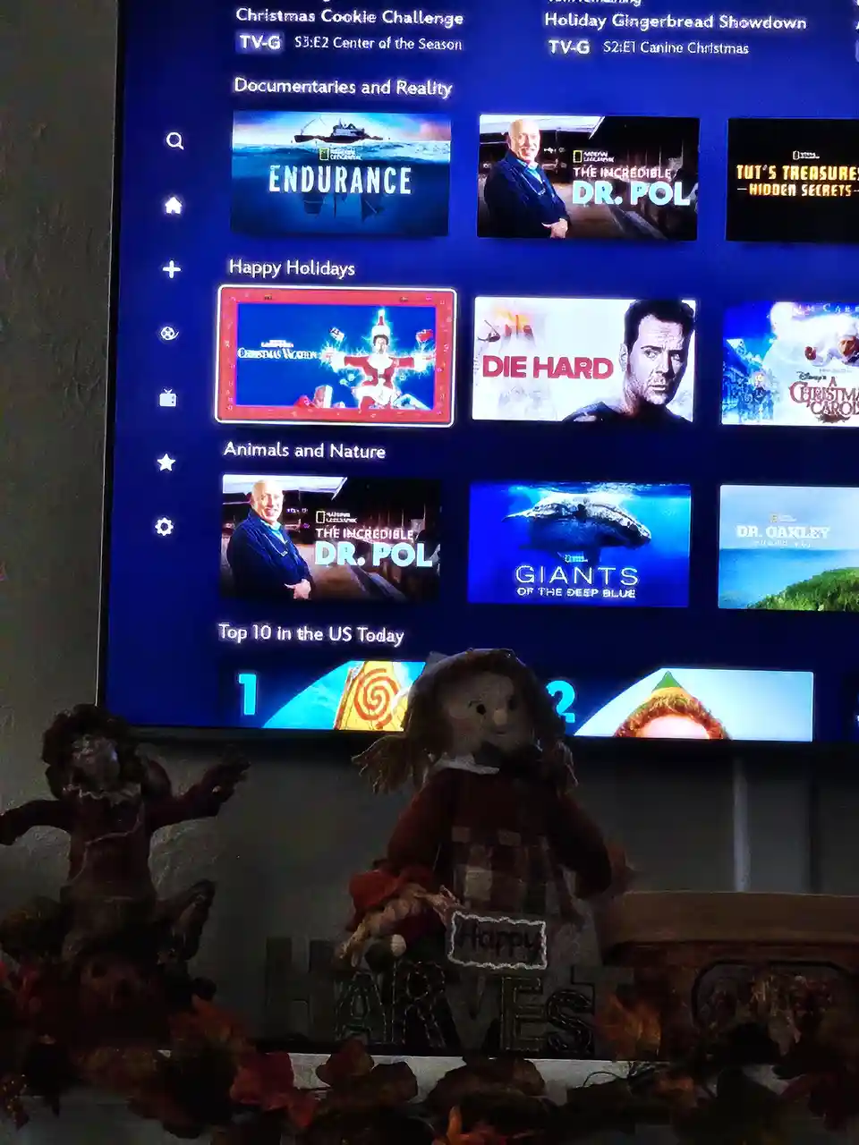 A television screen displays a streaming service interface with holiday-themed content, including 'Die Hard' under the…
