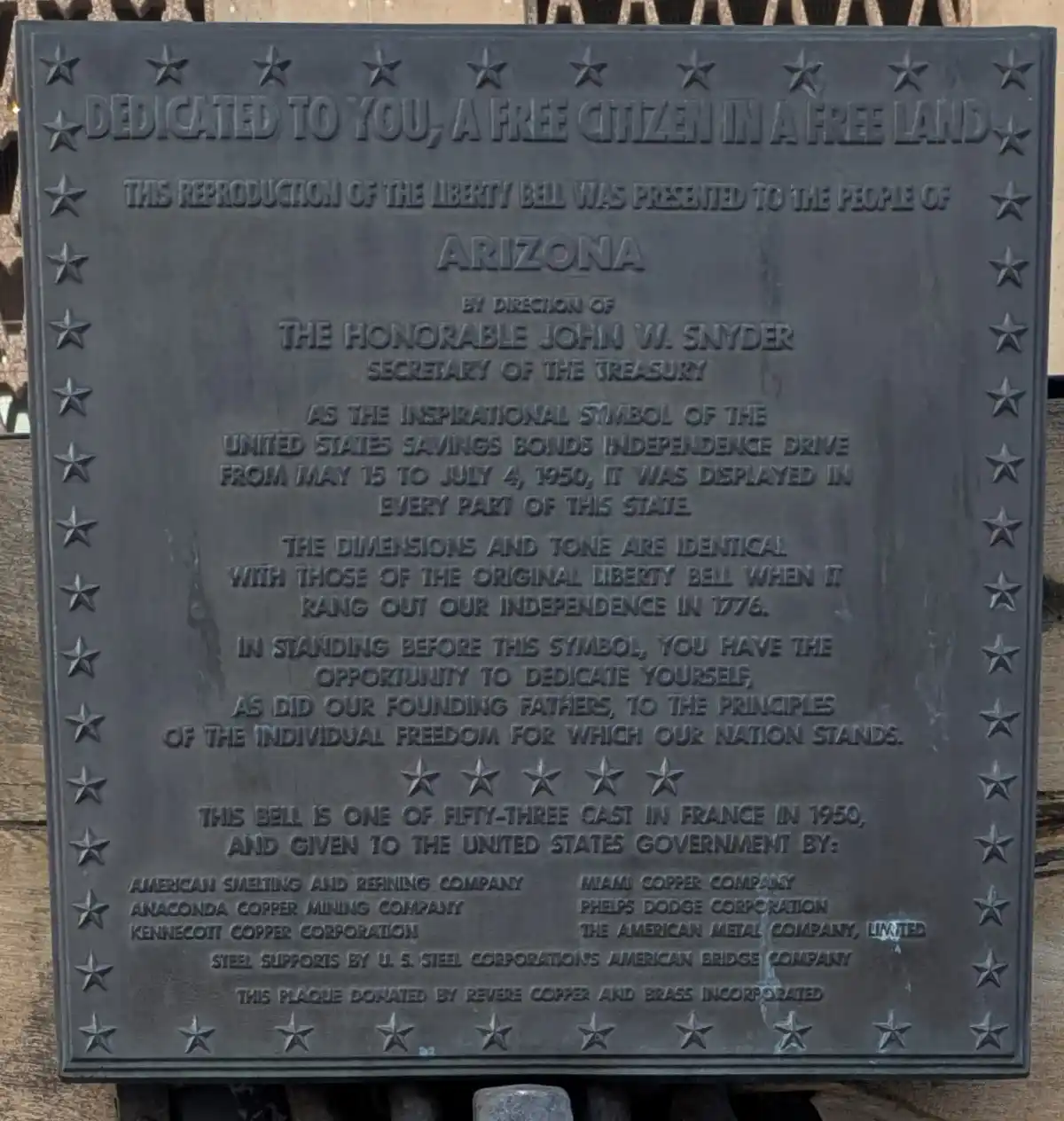 A close-up of a dark metal plaque with raised text and star borders, detailing a reproduction of the Liberty Bell presented…