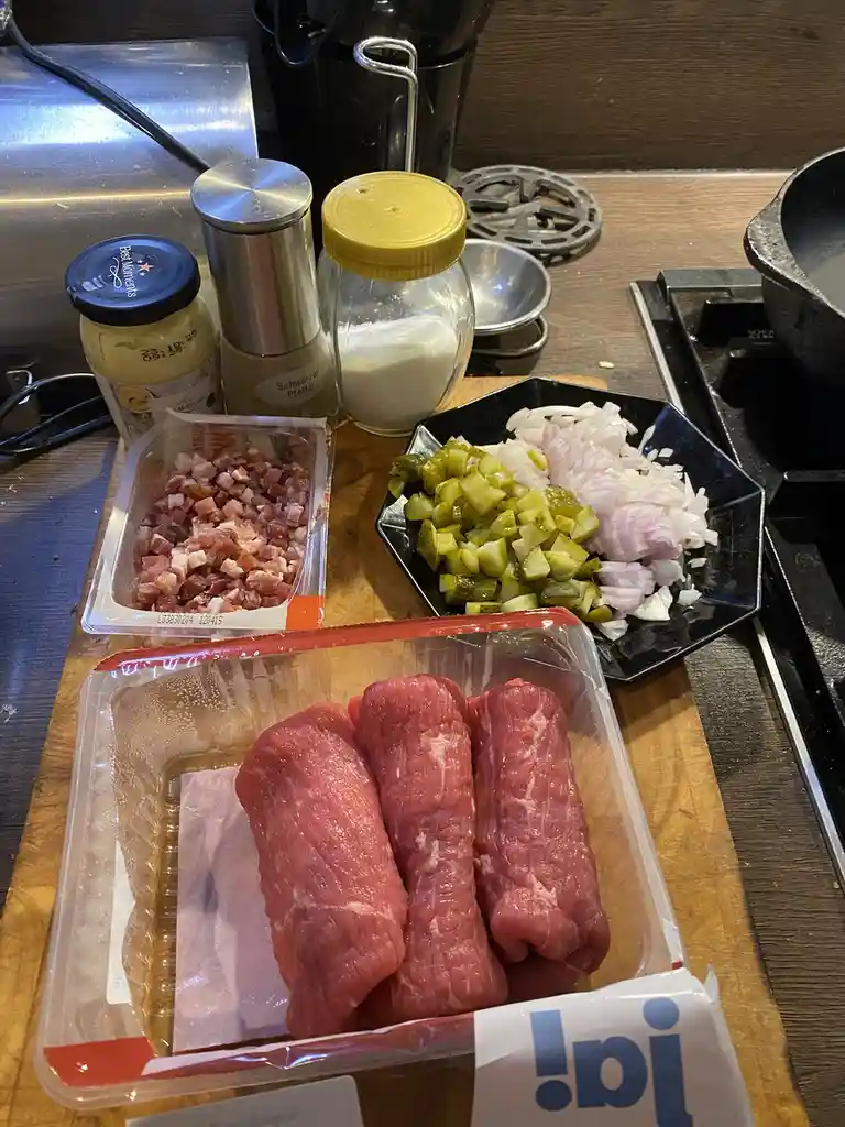 A kitchen counter displays raw meat, chopped onions, pickles, and spices in containers, with overlaid text reading 'i just…