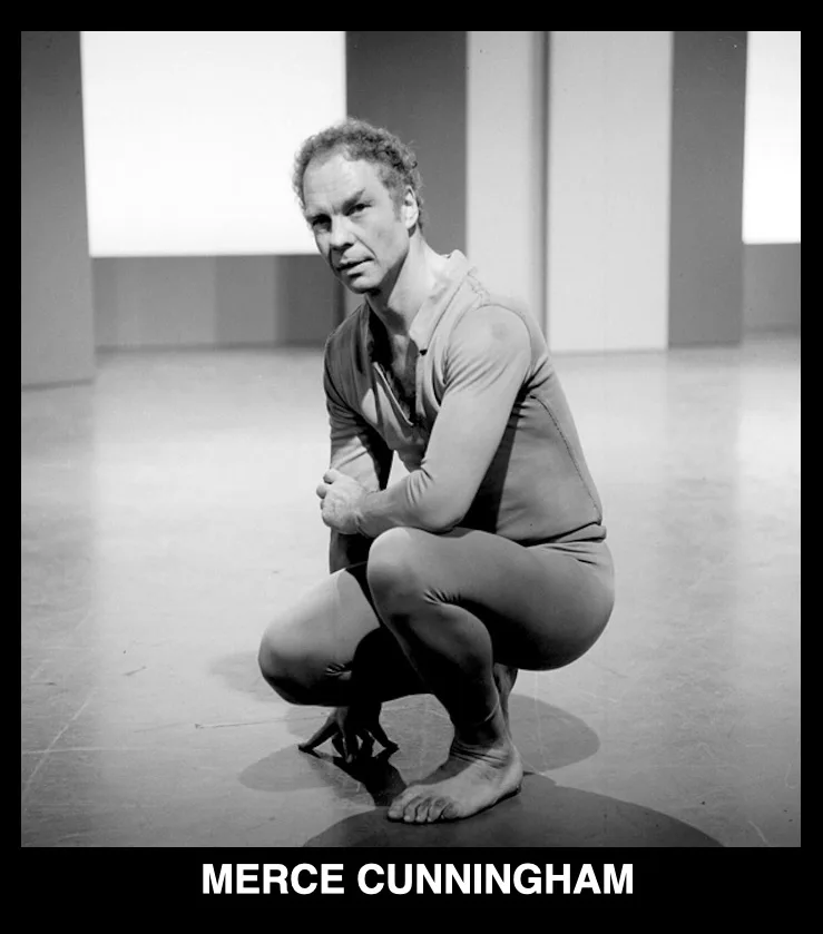 A black-and-white photograph shows a man in a form-fitting, long-sleeved leotard squatting on a bare floor with one foot…