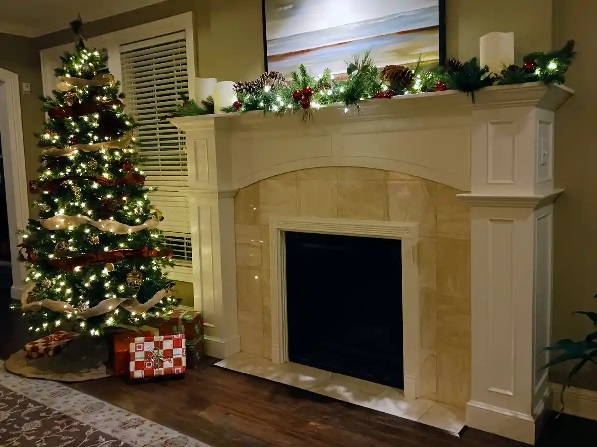 A warmly lit living room features a decorated Christmas tree with lights, ribbons, and presents underneath, positioned next…