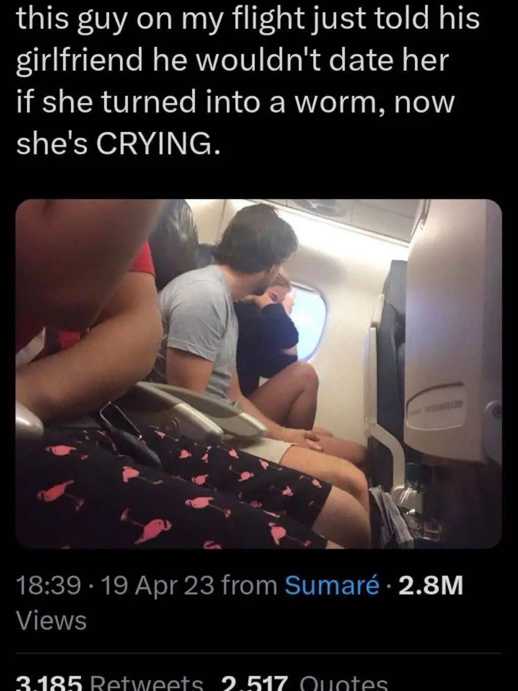 A man in a grey t-shirt sits on an airplane, leaning over and comforting a woman in a black top who is visibly crying while…