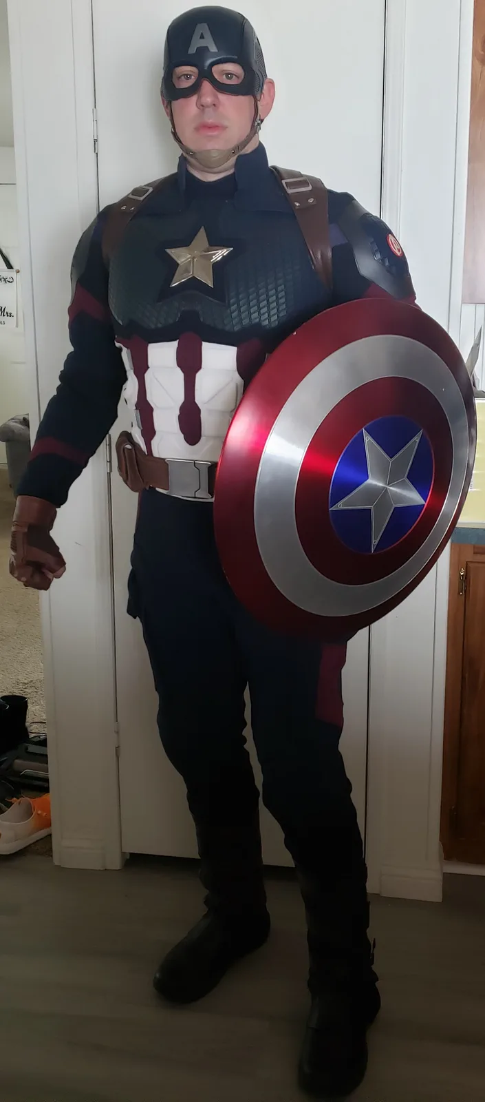 A man in a full Captain America costume, including helmet, star-emblazoned chest piece, and iconic red, white, and blue…