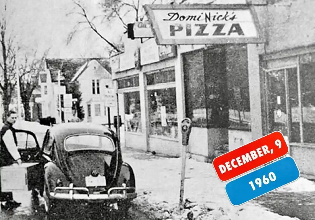 A black-and-white photo from December 9, 1960, shows a man standing beside a vintage Volkswagen Beetle on a snowy street…
