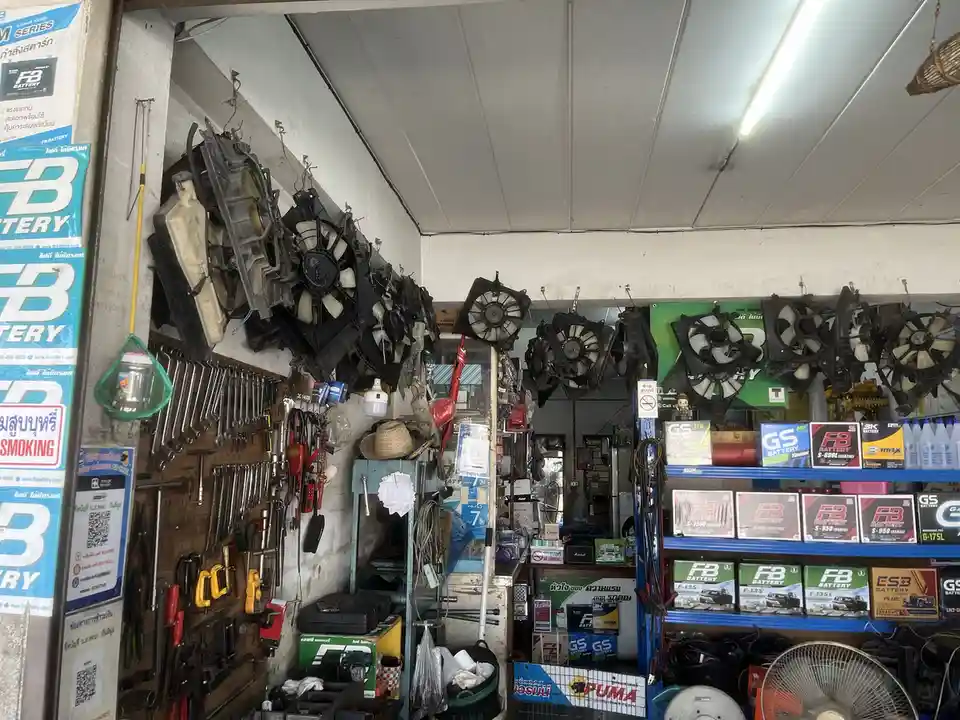 the image shows the interior of a cluttered auto parts shop with numerous used car radiators and cooling fans hanging on the…