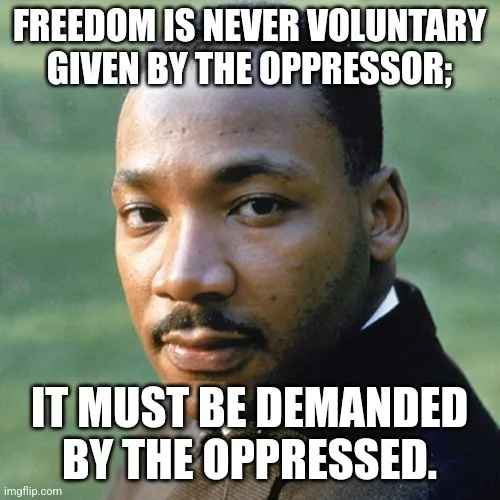 A close-up photo of Martin Luther King Jr. looking serious and direct at the viewer, with bold white text overlaid at the…