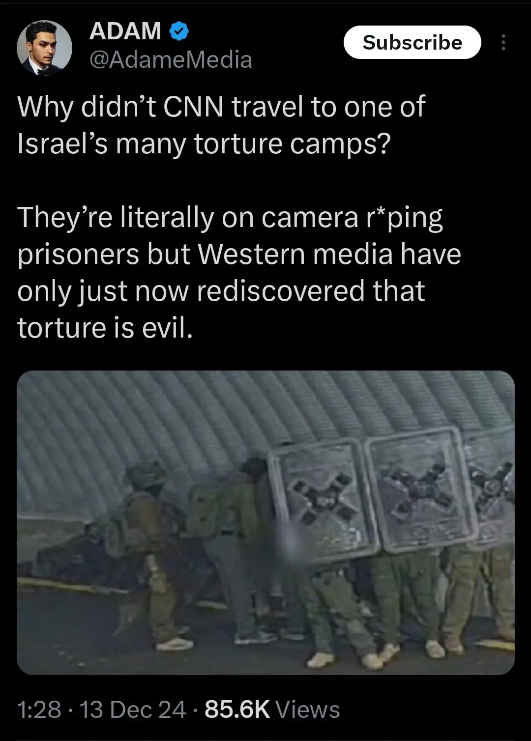 The image shows a low-resolution, grainy video still of several soldiers in uniform standing in a dimly lit, corrugated…