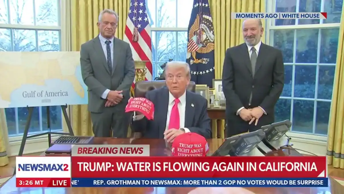 A still from a Newsmax2 broadcast shows Donald Trump seated at a desk in the Oval Office, holding a red 'TRUMP WAS RIGHT…