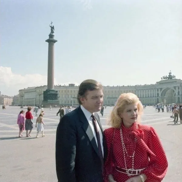A vintage photo shows a man in a dark suit and a woman in a red polka-dot dress standing together in a large public square…
