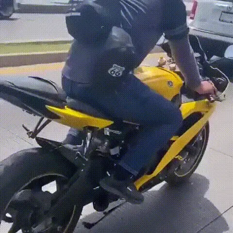 A six-panel sequence shows a man on a yellow motorcycle suddenly engulfed in flames while driving on a city street. The fire…