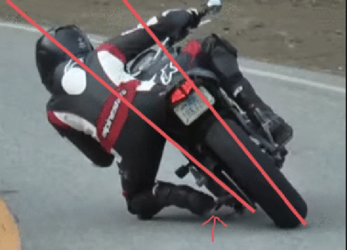 a motorcyclist in black and red gear is leaning extremely far into a turn on a road, with red diagonal lines crossing over…