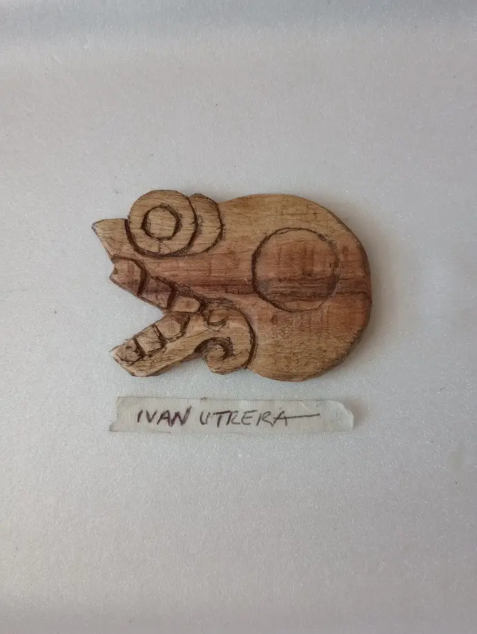 A small, hand-carved wooden figurine resembling a stylized animal or mythical creature with circular eyes and an open mouth…