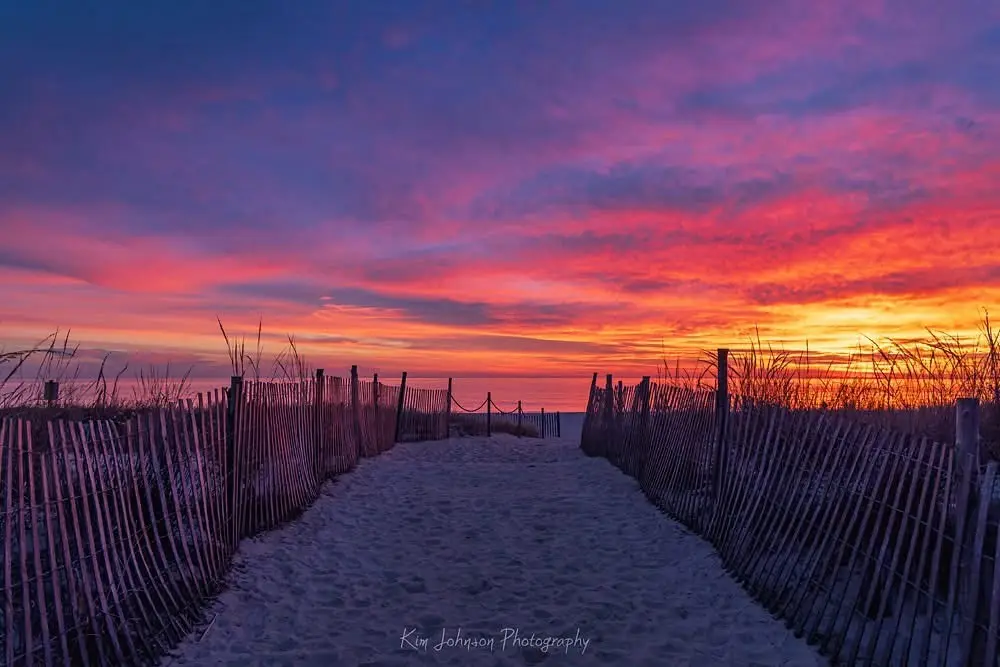 A serene beach sunset photo with a wooden fence-lined path leading to the ocean, overlaid with the text 'i'm not lazy, i'm…