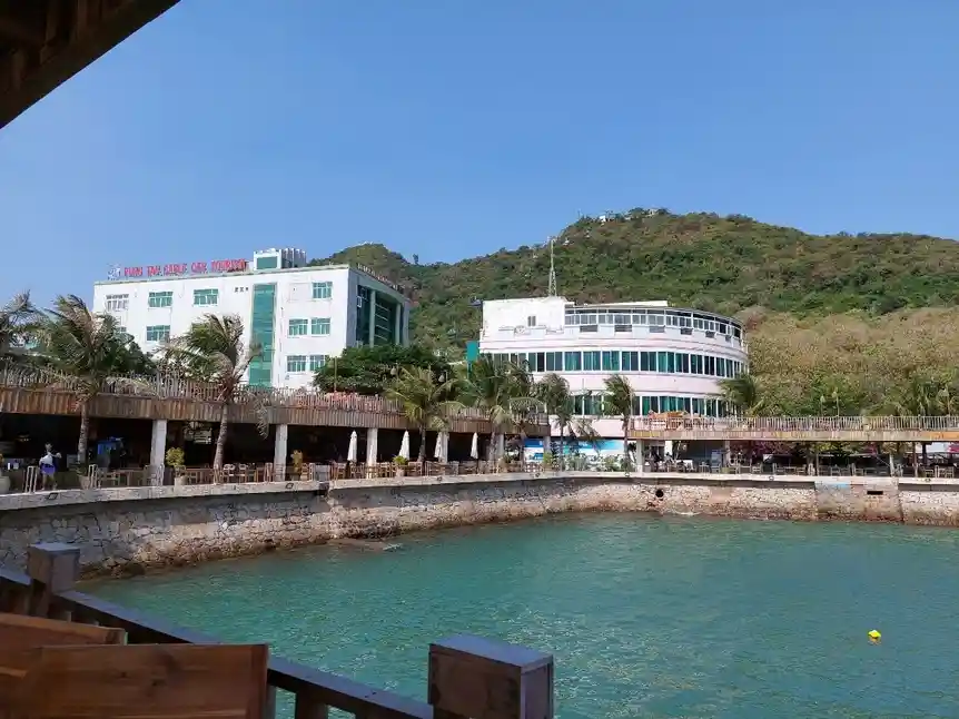 A scenic photo of a tropical waterfront with modern buildings, palm trees, and turquoise water under a clear blue sky…