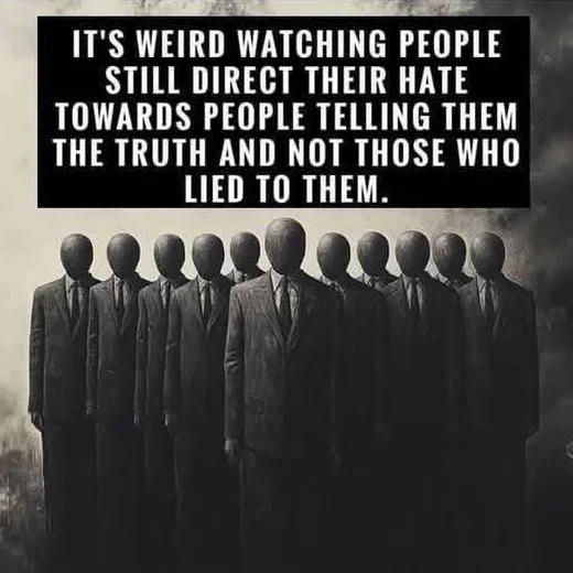 A black-and-white image shows a line of identical, faceless figures in dark suits standing in a row against a smoky, ominous…