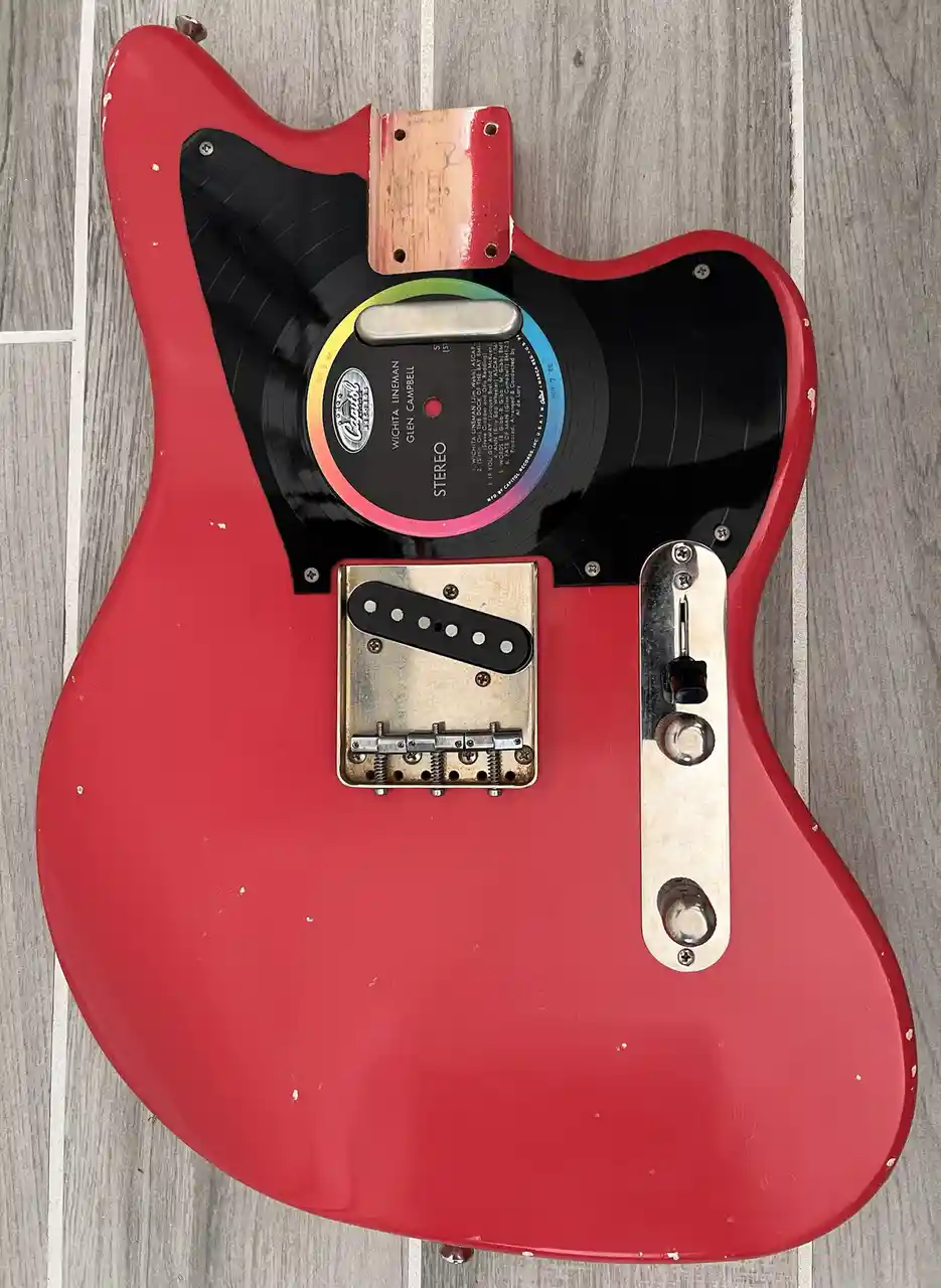 A red electric guitar with a black pickguard replaced by a vinyl record, showing the label for 'Wichita Lineman' by Glen…