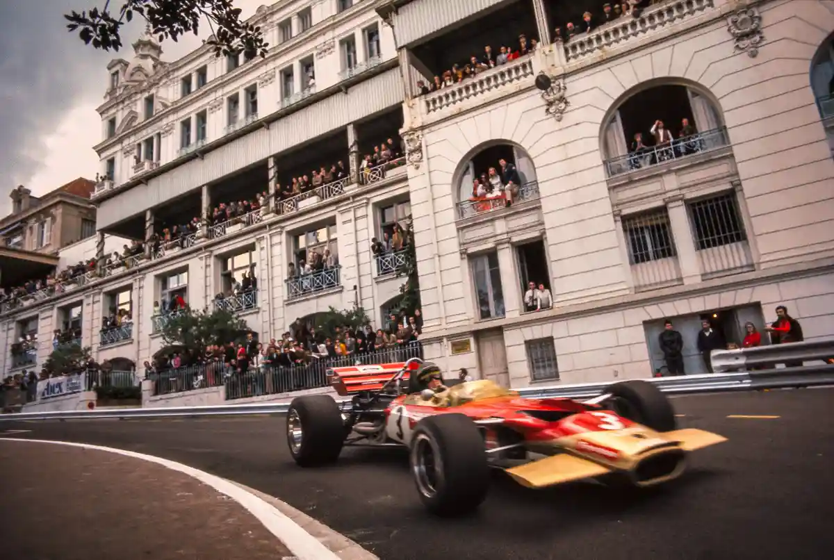 A vintage red and gold Formula 1 race car, number 3, speeds along a curving street lined with grand white buildings…