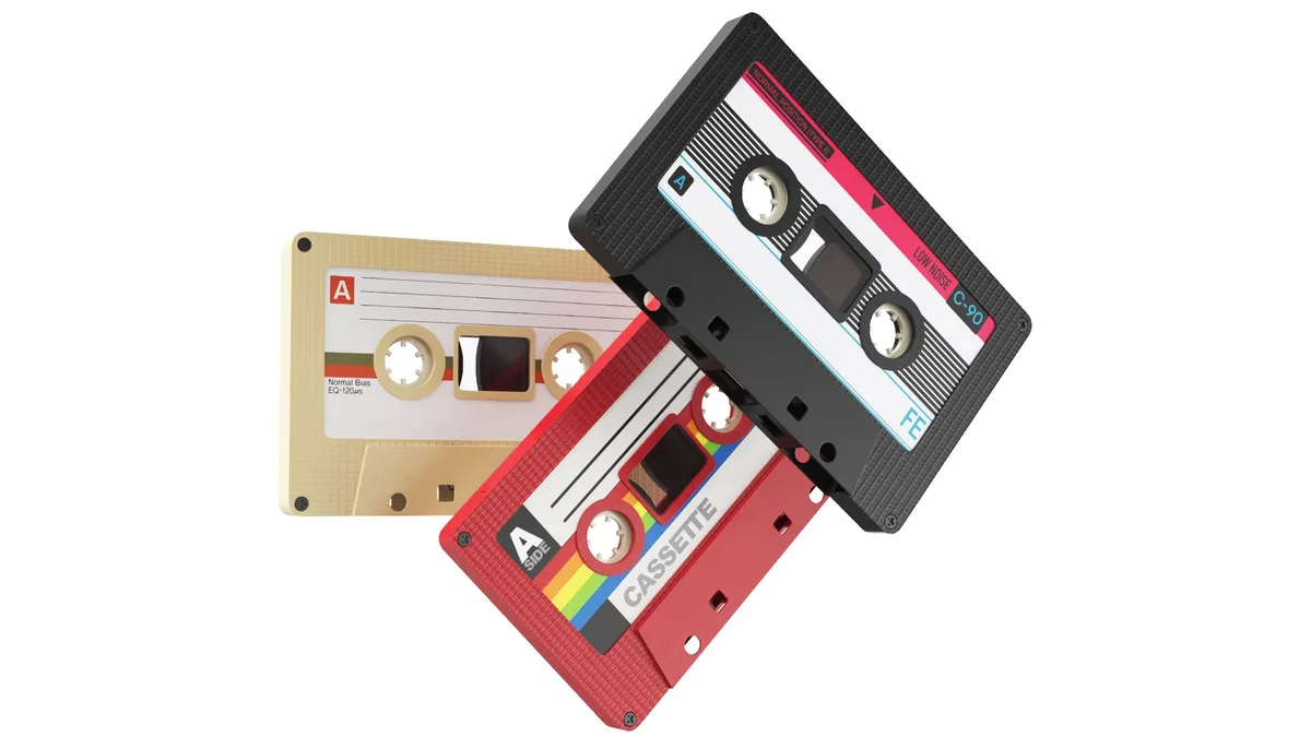 Three vintage audio cassette tapes are stacked diagonally against a white background. One is black with pink and blue…