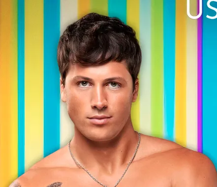 A shirtless man with dark hair and a silver chain necklace stares directly at the camera against a vibrant, multicolored…