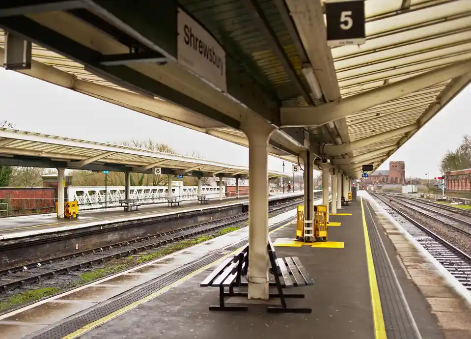 An empty train station platform at Shrewsbury, with visible platform numbers 5 and 6, benches, tracks, and a distant church…