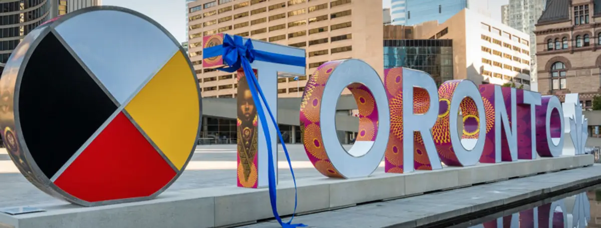 A large, colorful 'TORONTO' sign with each letter decorated in vibrant, patterned designs stands beside a circular…