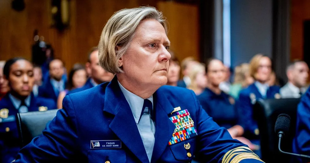 a woman in a blue U.S. Coast Guard uniform with name tag 'FADAN' and numerous medals sits in a formal hearing room, looking…