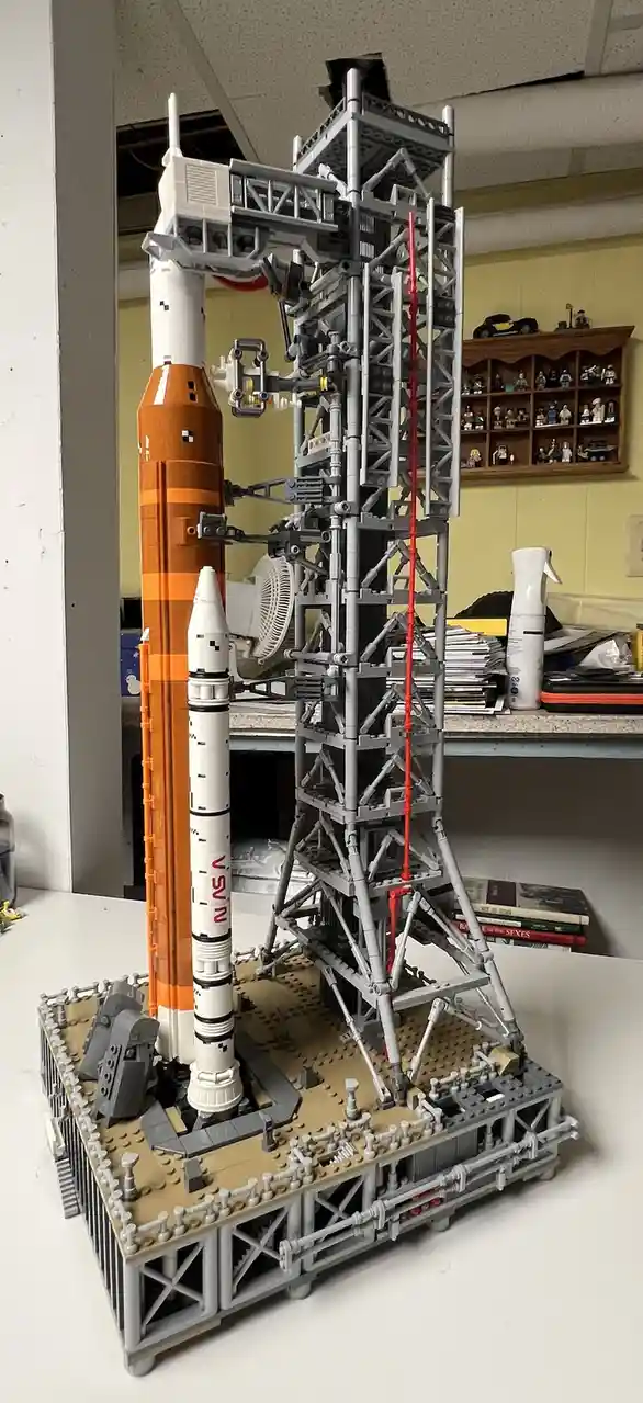 A highly detailed LEGO model of a rocket on a launchpad, featuring an orange and white rocket with 'NASA' written on it…