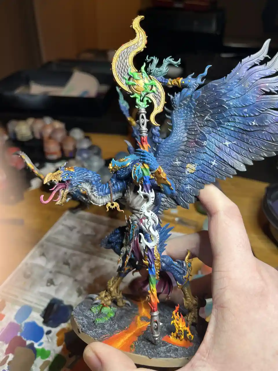 A hand holds up a highly detailed, intricately painted fantasy miniature of a blue-winged, multi-headed dragon-like creature…