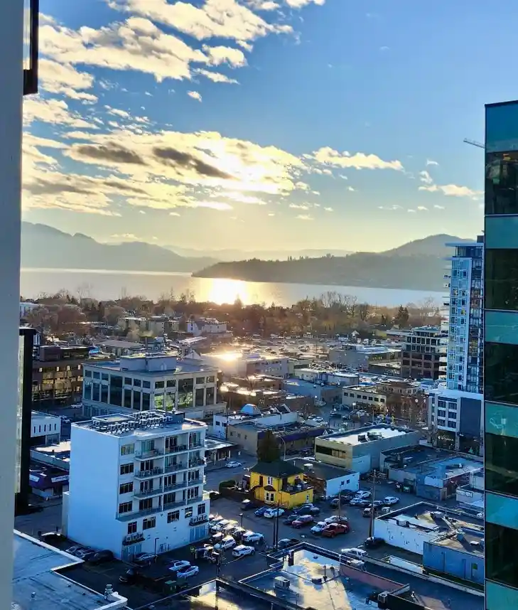 A scenic daytime photo from a high-rise apartment window shows a sprawling urban landscape with buildings, parked cars, and…