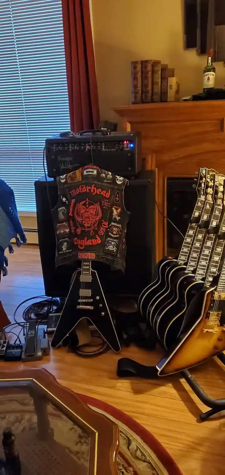 A black electric guitar with a distinctive pointed body shape stands upright on a wooden floor, with a heavily patched black…