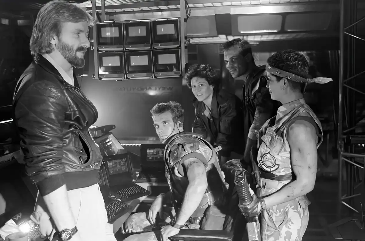 A black-and-white photo shows five people in a sci-fi spaceship control room, with one man in a leather jacket standing and…