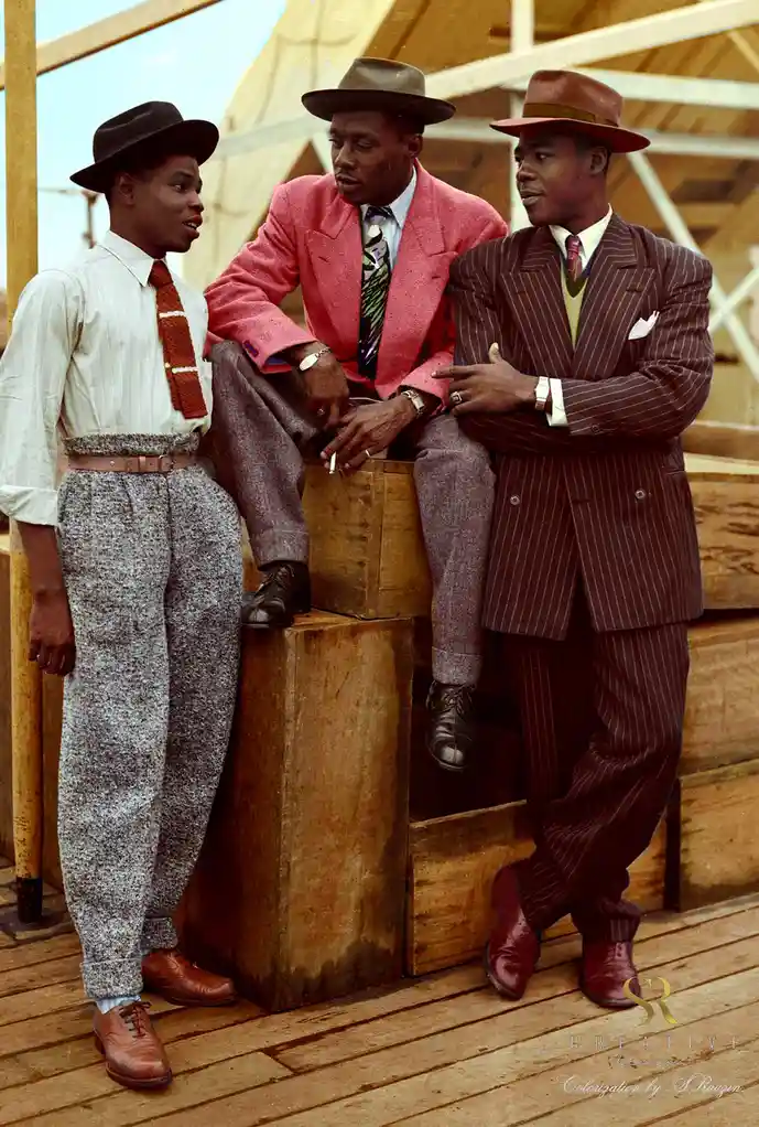 Three stylish Black men in 1940s fashion pose on wooden crates; one in a pink suit holds a cigarette, another in a pinstripe…