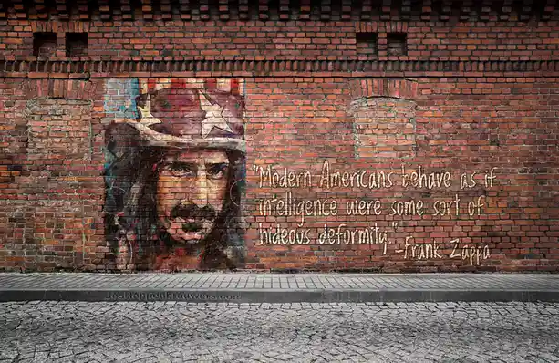 A mural on a red brick wall depicts a portrait of Frank Zappa wearing a star-spangled hat, next to his quote about modern…