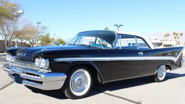 A black 1950s Chevrolet with chrome trim and white-wall tires is parked outdoors under a clear blue sky. The overlaid text…