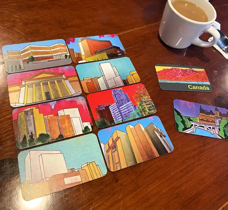 Several illustrated postcard-style cards depicting various buildings and landscapes are scattered on a wooden table next to…