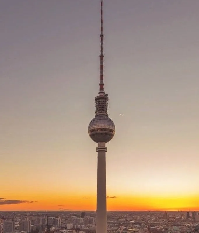 A tall, slender tower with a spherical observation deck near the top, set against a sunset sky with orange and purple hues…