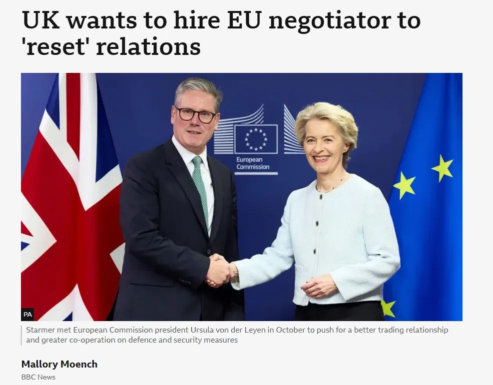 A photo shows two political figures shaking hands in front of a blue backdrop with the European Commission logo, a British…