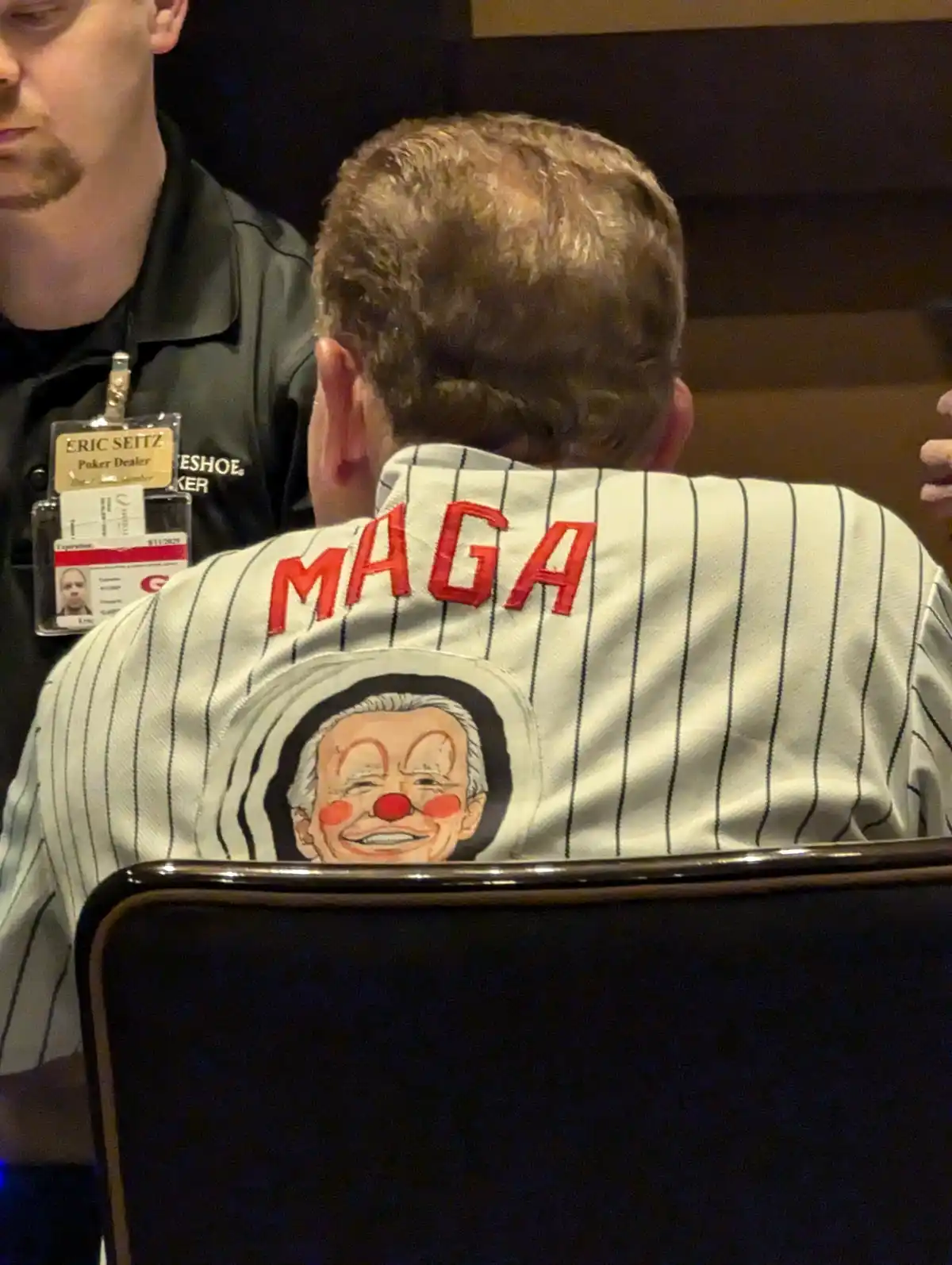 A person is seen from behind wearing a white pinstripe baseball jersey with 'MAGA' in red letters across the shoulders and a…