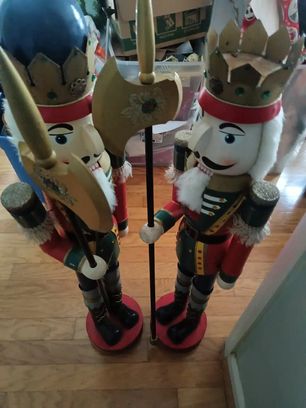 Two large, ornate nutcracker figurines stand side by side on a wooden floor, both wearing crowns and holding weapons. The…