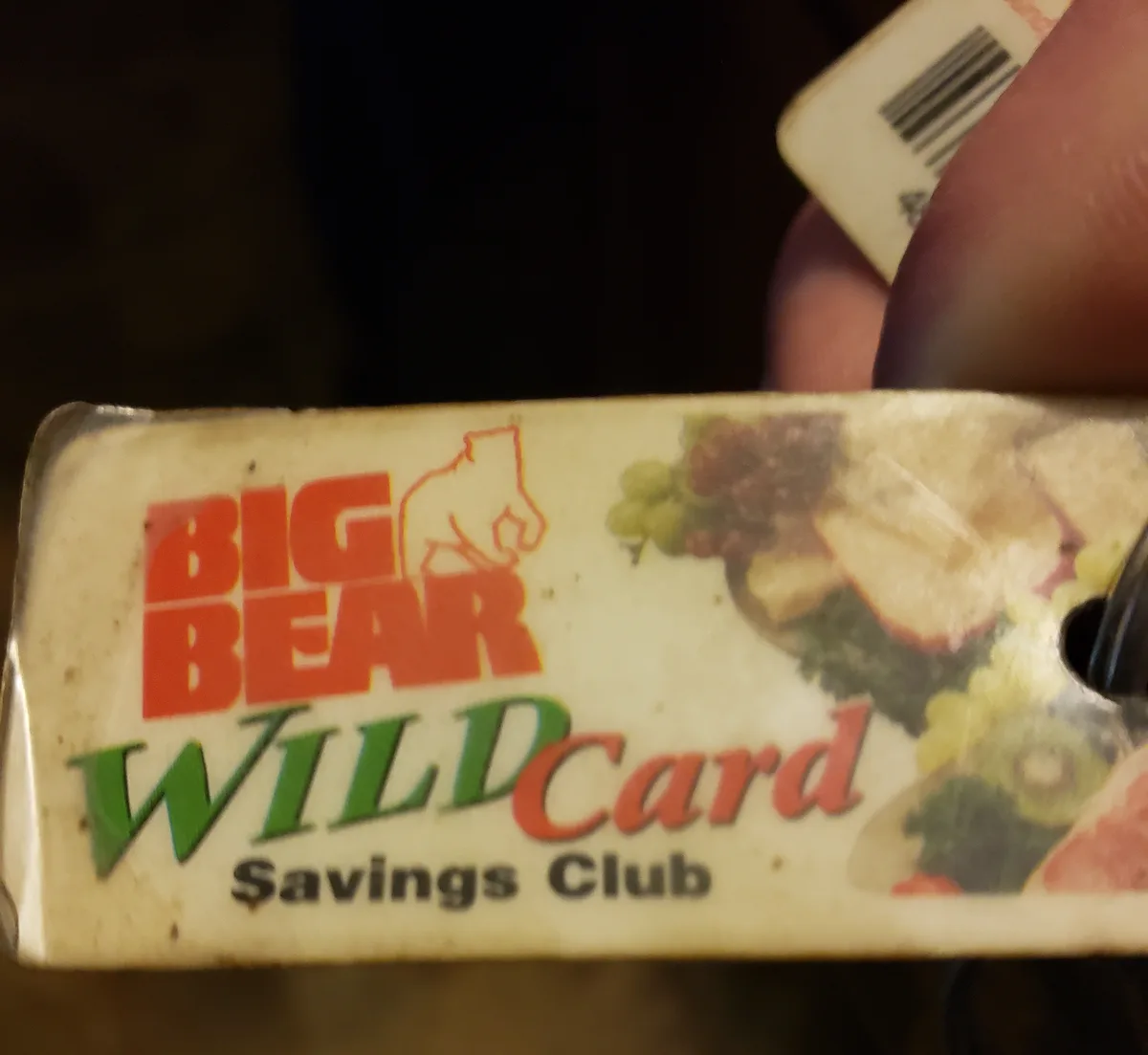A close-up photo shows a person's fingers holding a worn plastic card with 'BIG BEAR WILDCARD Savings Club' printed on it in…