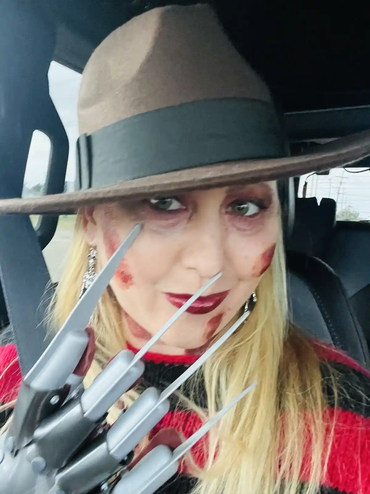 A woman dressed as Freddy Krueger, wearing a brown fedora, red and black striped sweater, and a glove with metal blades…